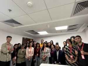 Group of diverse people wearing red lanyards posing for a group photo in a conference room indoors.