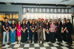 Group of diverse young professionals posing for a photo in a modern lobby, all wearing red lanyards and name badges.