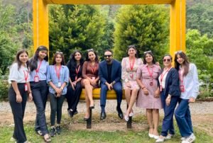 Group of ten adults posing on a bright yellow swing frame outdoors, wearing business casual clothes and red lanyards, with greenery in the background.