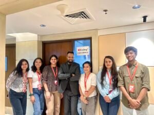 Group of colleagues posing in an office lobby outside a door marked 'Foxhog CEO Office' with red lanyards and ID badges.