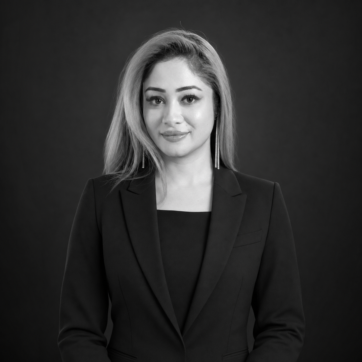 Professional woman in a black blazer posing for a studio portrait against a dark background.