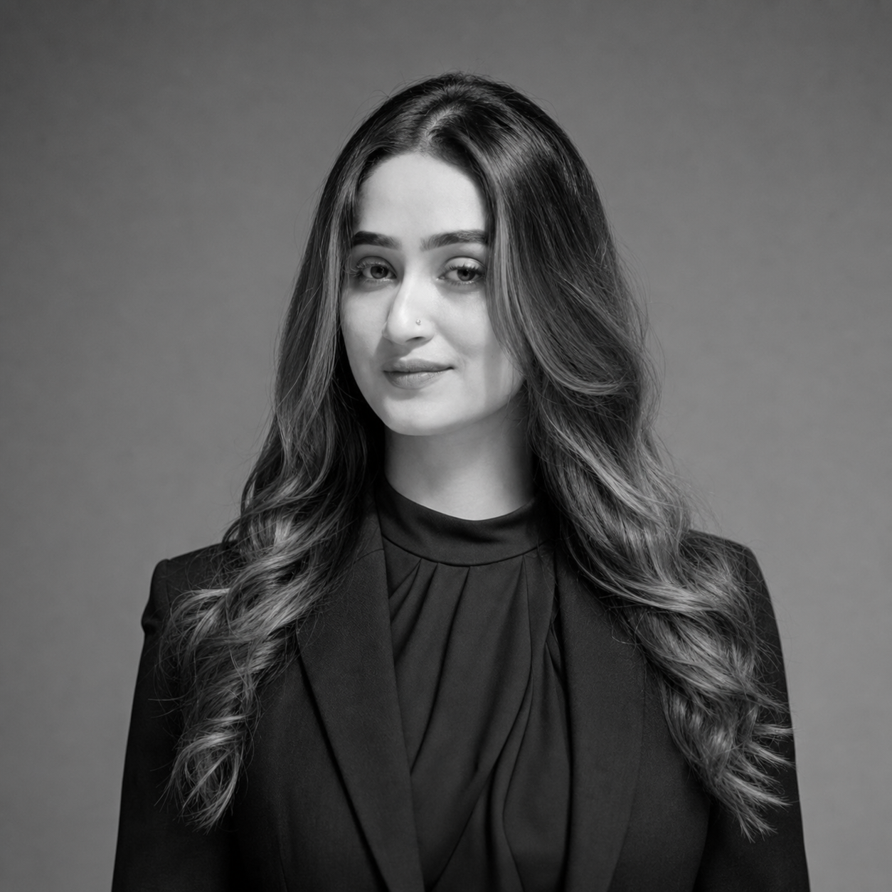 Black-and-white portrait of a woman with long wavy hair, wearing a dark blazer and blouse, facing slightly left against a neutral backdrop.