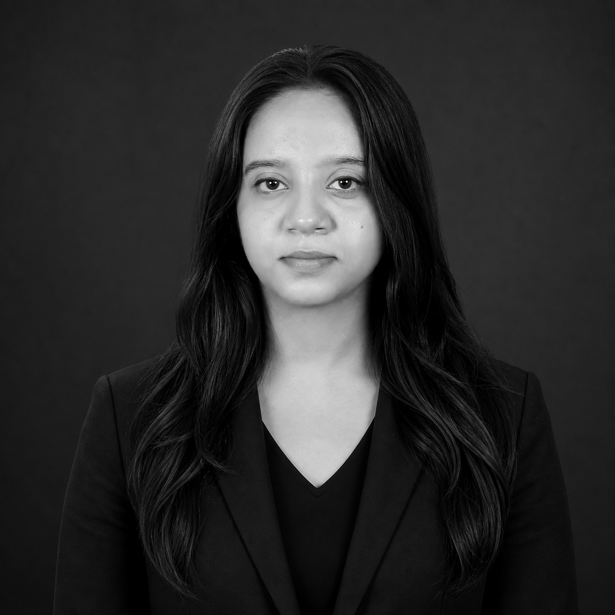 Front-facing, black-and-white headshot of a woman in a blazer against a dark backdrop.