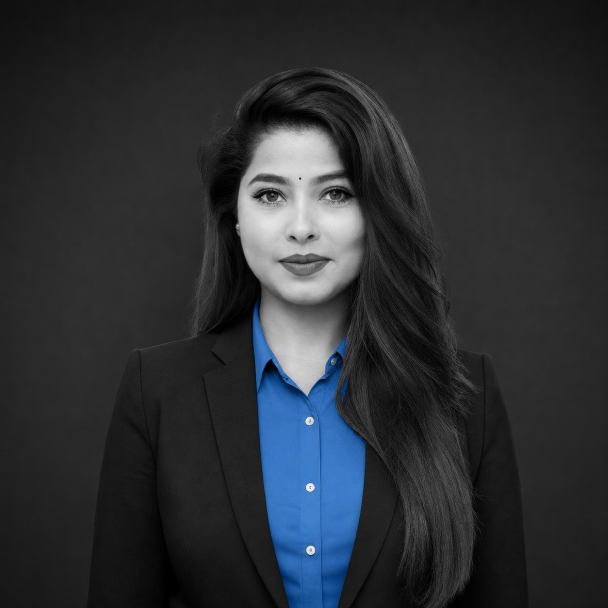 Professional headshot of a woman with long dark hair, wearing a blue blouse and black blazer against a dark backdrop.