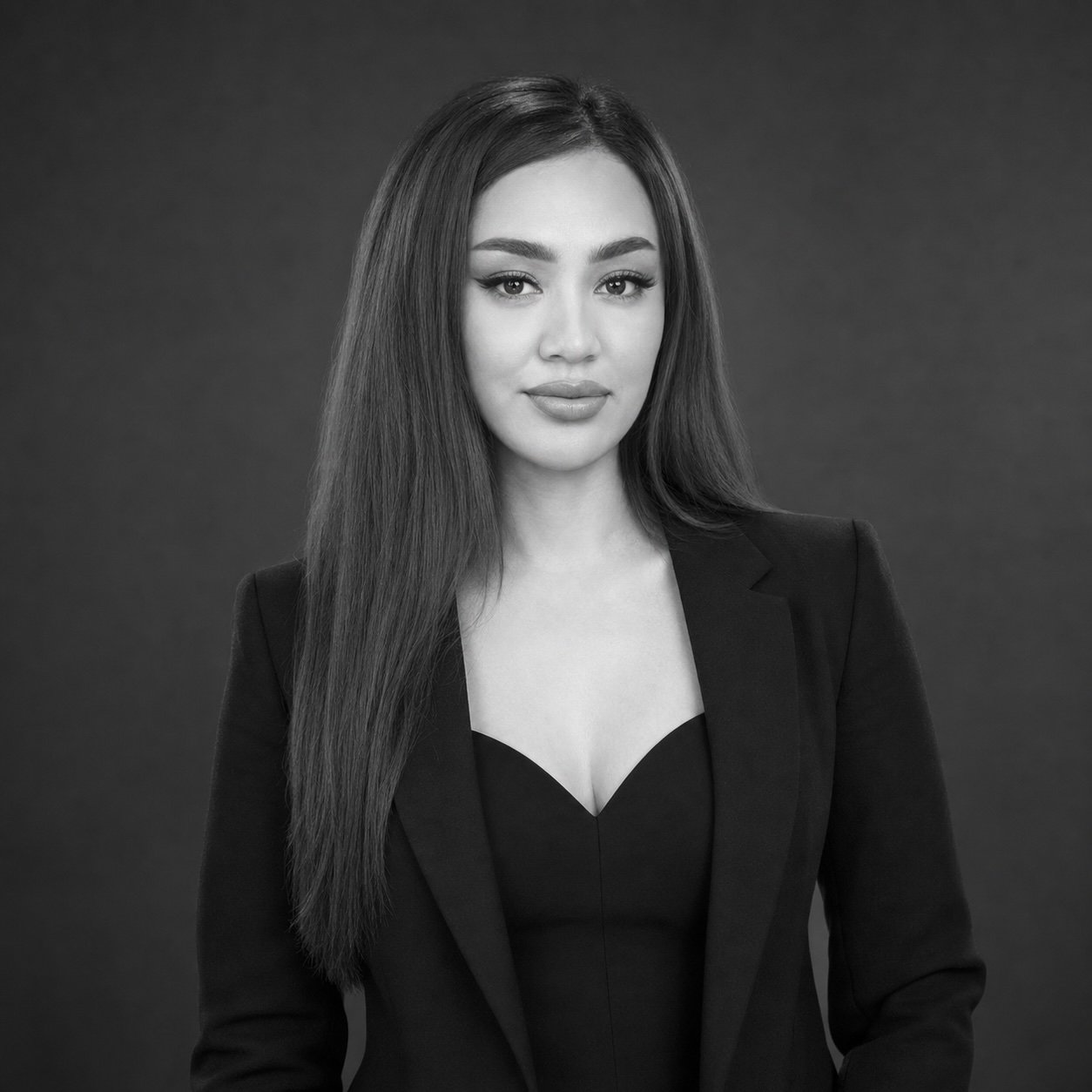 Professional head-and-shoulders portrait of a woman with long dark hair, wearing a black blazer, facing the camera in a studio.
