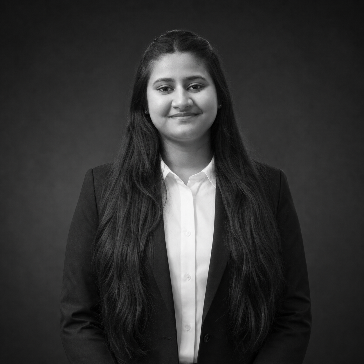 Professional head-and-shoulders portrait of a woman with long dark hair, wearing a black blazer and white button-down shirt, smiling softly against a dark backdrop.