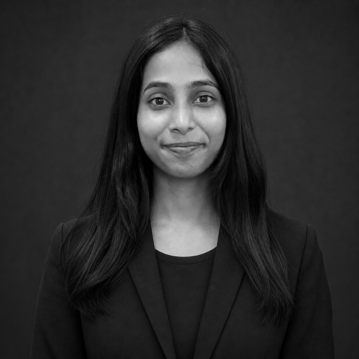 Professional headshot of a woman with long dark hair, wearing a black blazer, and a subtle smile. Possibly a corporate portrait.