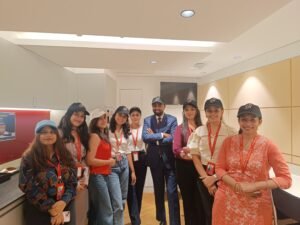 Group of diverse colleagues wearing lanyards pose for a team photo in a modern office kitchen area.