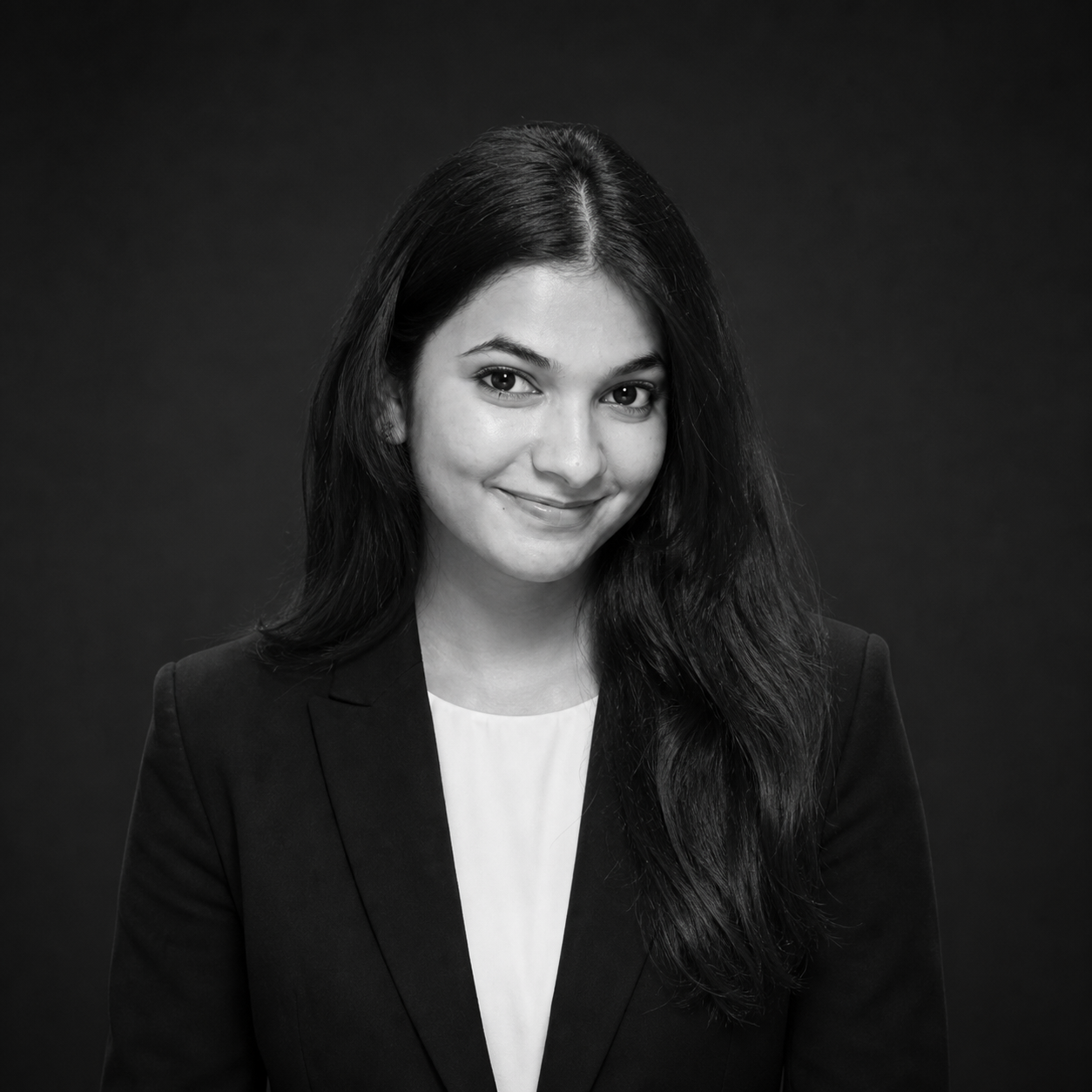 Black-and-white headshot of a smiling woman in a blazer against a dark backdrop.