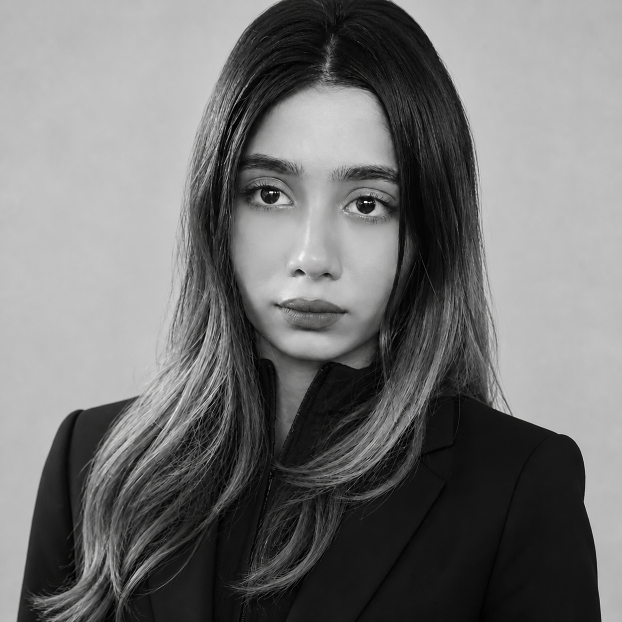 Black-and-white portrait of a young woman with long dark hair wearing a blazer, looking at the camera.
