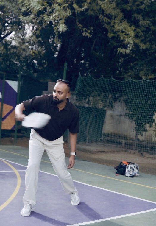 Man in a black polo and white pants throws a white disc on a purple outdoor court; a bag sits on the court nearby