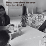 People in a business discussion around a table; a QR code card sits on the table, Foxhog logo top-right, captioned about assessing startup risk.