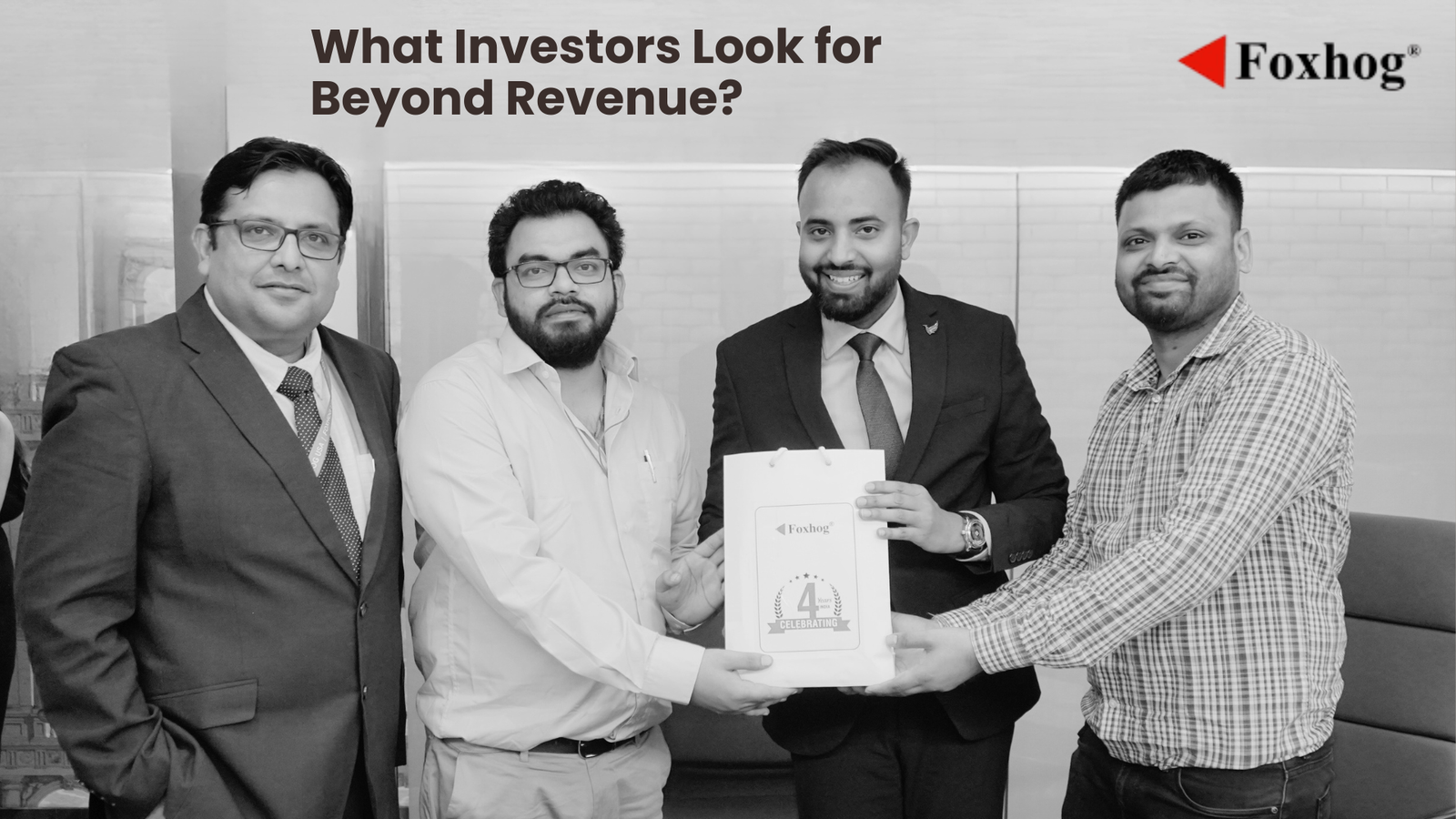 Four men in business attire pose together as one hands a certificate to another, Foxhog logo visible in the background (black and white photo).