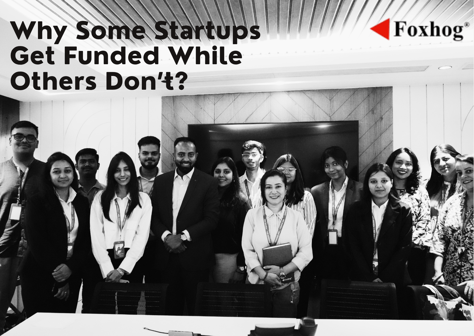 Group of professionals posing in an office with a large banner reading 'Why Some Startups Get Funded While Others Don’t?' and the Foxhog logo ahead of them.