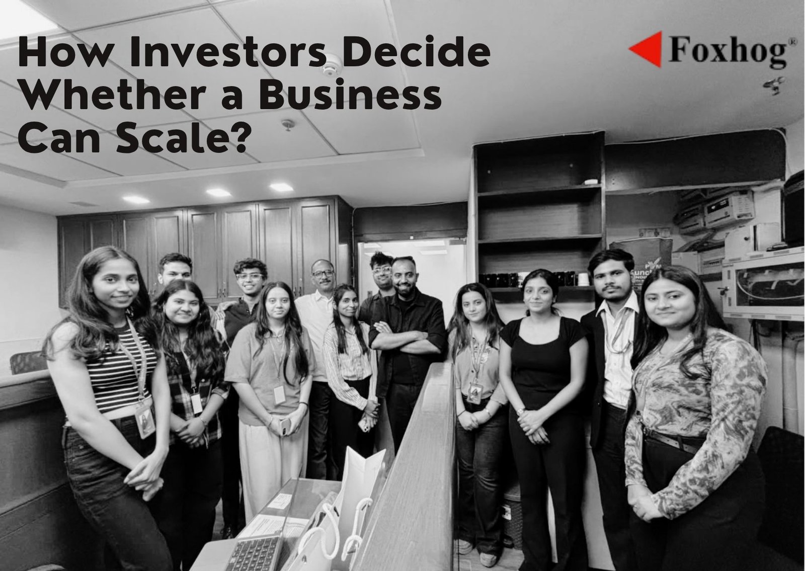 Group of diverse professionals in an office with a long conference counter; article title 'How Investors Decide Whether a Business Can Scale?' and Foxhog logo top right.